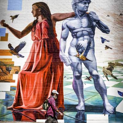 man walks in front of large public mural