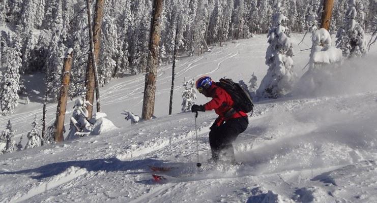 A skier in a red jacket descends down a snowy mountain slope, kicking up snow behind his skis in Flagstaff, Arizona