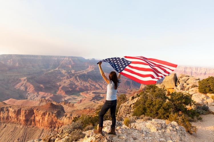 A woman stands on the edge of the Grand Canyon while holding an American flag above her head near Flagstaff, AZ.