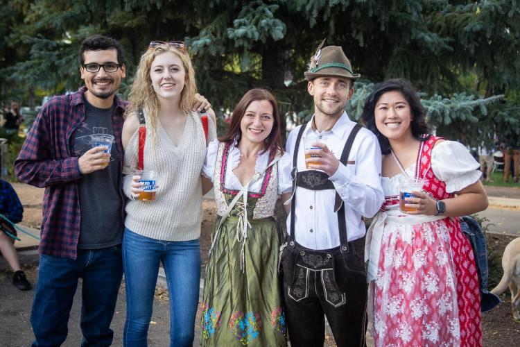 A group of people, three of which are in traditional German dress, hold cups of beer at an Oktoberfest celebration.
