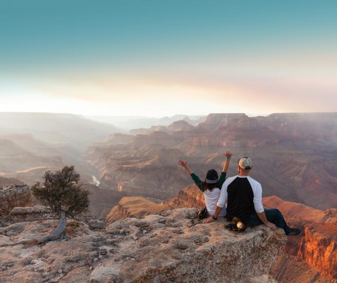 a man and woman sit on the edge of the Grand Canyon and look off into the distance