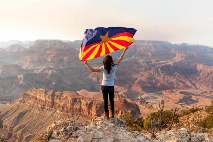 woman holding arizona flag at the rim of grand canyon