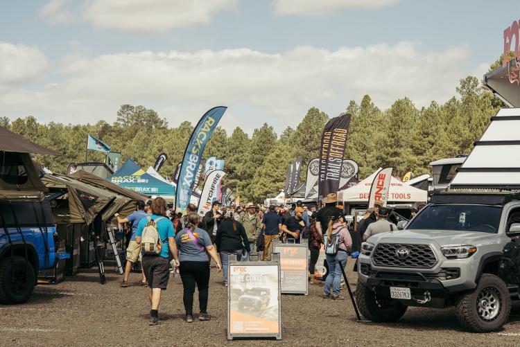 A large crowd of people visit vendor booths and look at cars at the Overland Expo