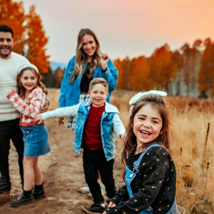 family of five have fun taking photos in a field surrounded by orange and red fall foliage