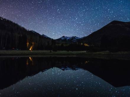 Stars reflect off of a lake surrounded by pine trees and mountains at Lockett Meadow. Photo Credit: @deborahsoltesz