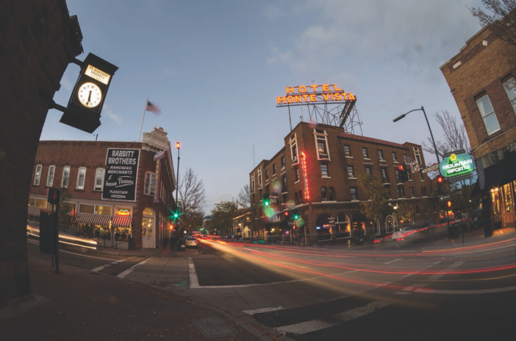 View of cars driving through the streets of Downtown Flagstaff in the evening. the Hotel Monte Vista sign glows