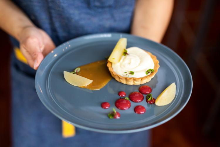 A person holds a blue plate featuring a beautifully plated dessert at Shift Kitchen and Bar
