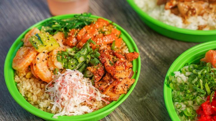 A green bowl with various seafood and poke bowl toppings