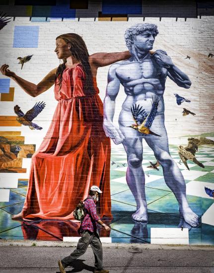 man walks in front of large public mural