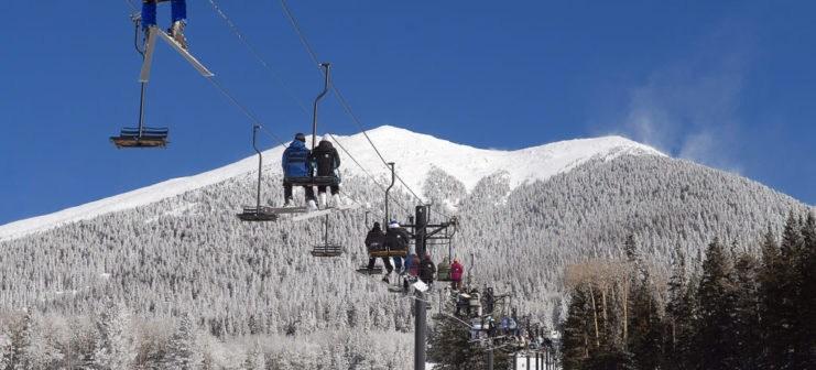 Skiers and snowboarders sit on a chairlift as they move towards a snow-covered summit in Flagstaff, Arizona.