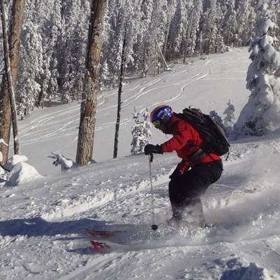 A skier in a red jacket descends down a snowy mountain slope, kicking up snow behind his skis in Flagstaff, Arizona