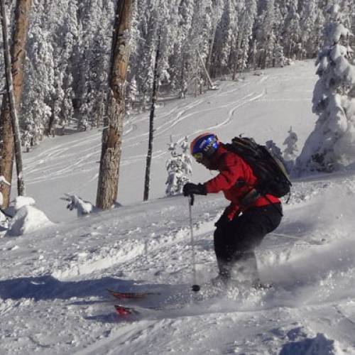 A skier in a red jacket descends down a snowy mountain slope, kicking up snow behind his skis in Flagstaff, Arizona