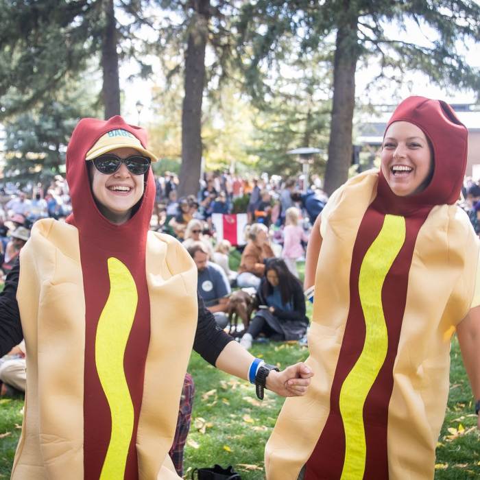 Two Oktoberfest attendees dressed as hot dogs stand in a park in Flagstaff, AZ.