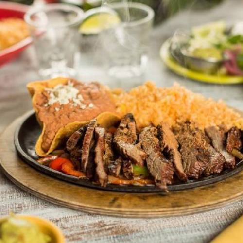 A plate of fajitas surrounded by colorful ceramic bowls