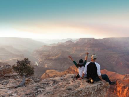 a man and woman sit on the edge of the Grand Canyon and look off into the distance
