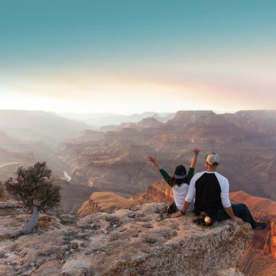a man and woman sit on the edge of the Grand Canyon and look off into the distance