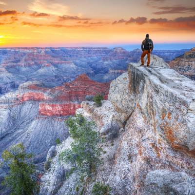 Man with backpack on rim of Grand Canyon with a colorful sunset in the background