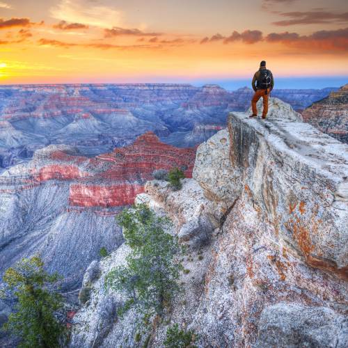 Man with backpack on rim of Grand Canyon with a colorful sunset in the background