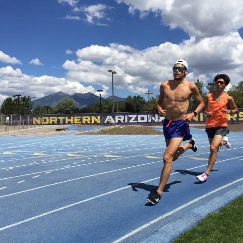 Two people running on the outdoor track at Northern Arizona University. Mountains are in the distance