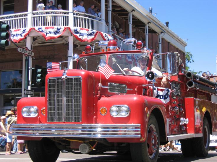 Bright red vintage firetruck decorated with flags riding through July 4th Parade route in Flagstaff, AZ