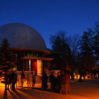 People walk around the Lowell Observatory at night. The observatory is a silhouette against the night sky