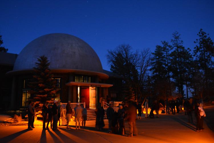 People walk around the Lowell Observatory at night. The observatory is a silhouette against the night sky