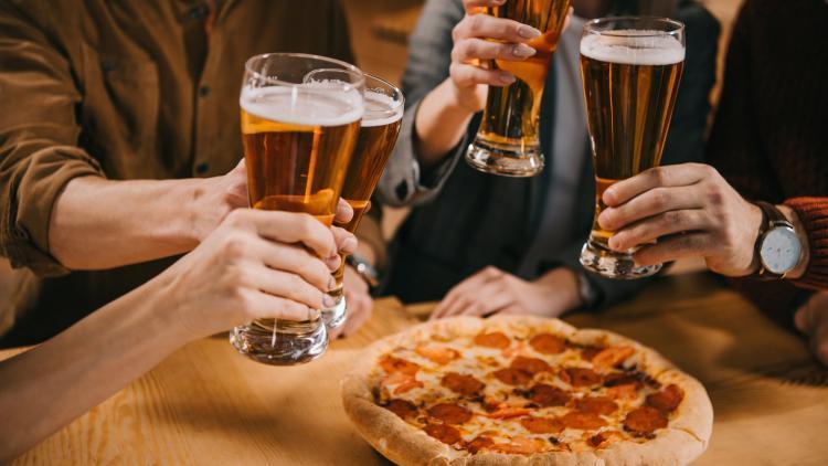 Three people raise tall glasses of beer over a pizza pie at Lumberjack Pizza in Flagstaff