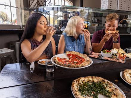 A group of friends bite into slices of pizza at Pizzicletta.