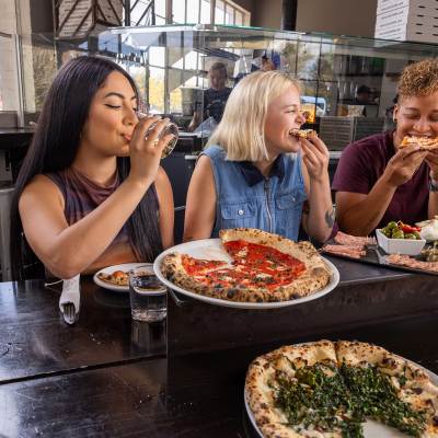 A group of friends bite into slices of pizza at Pizzicletta.