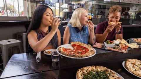 A group of friends bite into slices of pizza at Pizzicletta.