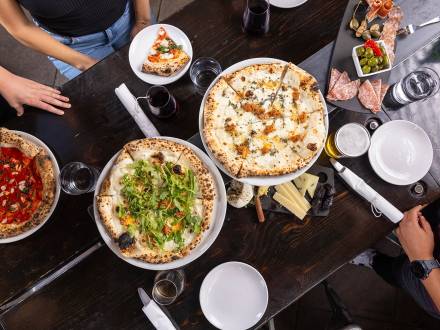 Different pizzas are placed on a dark wooden table at Pizzicletta.
