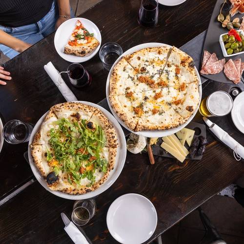 Different pizzas are placed on a dark wooden table at Pizzicletta.