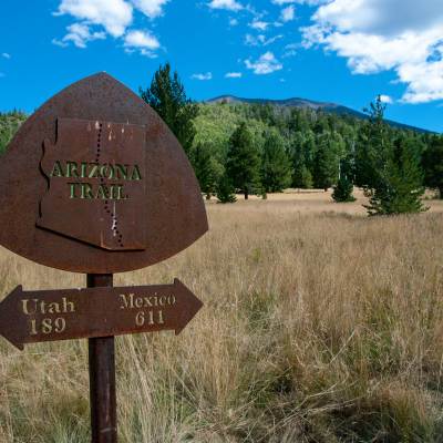 Rusted metal Arizona Trail trail marker with a double arrow sign underneath pointing to Utah and Mexico.