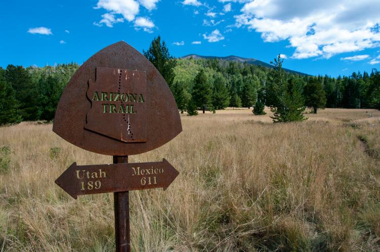 Rusted metal Arizona Trail trail marker with a double arrow sign underneath pointing to Utah and Mexico.