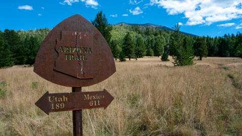 Rusted metal Arizona Trail trail marker with a double arrow sign underneath pointing to Utah and Mexico.