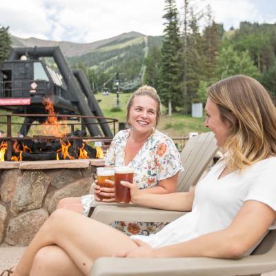 Two women enjoying pints of beer next to a bonfire at Arizona Snowbowl in Flagstaff, Arizona