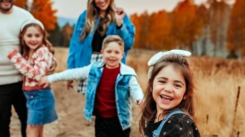 family of five have fun taking photos in a field surrounded by orange and red fall foliage