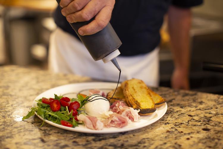 a chef prepares a plate of fresh mozzarella, prosciutto, salad and bread at Fat Olives