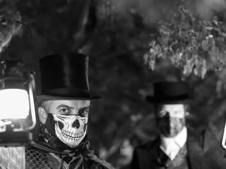 A tour guide from Freaky Foot Tours wears a top hat and skull face mask while carrying a lantern