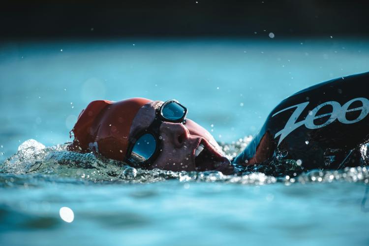 Close-up of a swimmer wearing goggles, swim cap, and swimwear, pops up for a breath mid-stroke