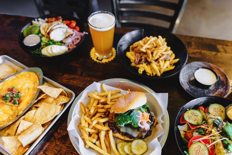 A glass of beer and a variety of dishes, including nachos, a burger, fries, and a salad from Lumberyard Brewing.