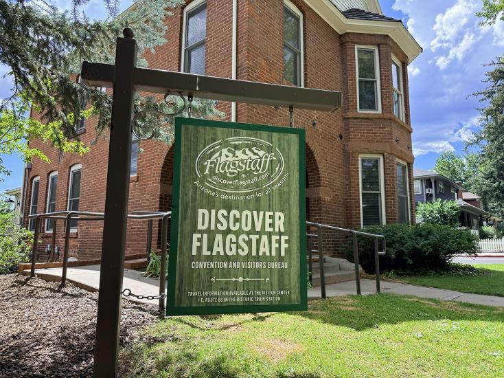 Green Discover Flagstaff sign outside on a green lawn with an old brick house in the background