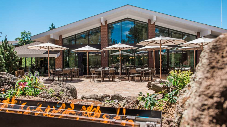 Outdoor patio at Little America Hotel on a sunny day. There are many tables with umbrellas and an outdoor fire