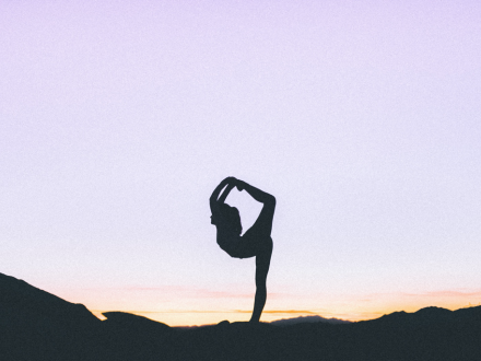 A woman does a yoga pose at sunrise in an outdoor setting.