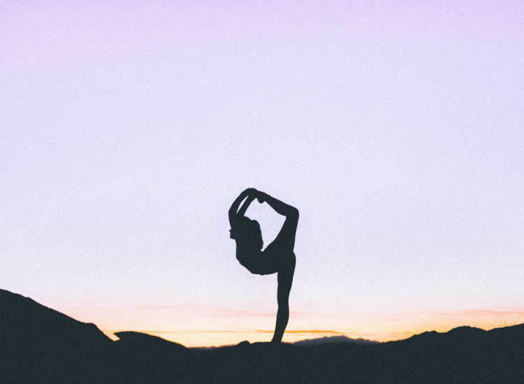 A woman does a yoga pose at sunrise in an outdoor setting.