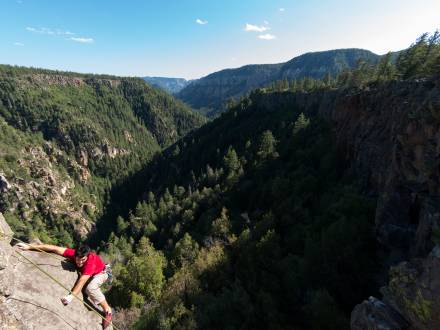 A person scales the cliffs of Oak Creek Canyon, which overlooks a vast forest.