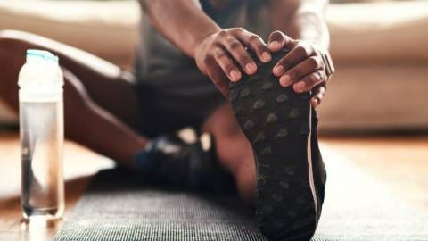 A person stretching their legs by sitting on the floor with one leg out and resting both hands on their foot